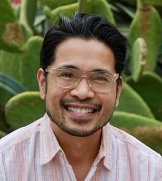 Person smiling with glasses against a cactus background.