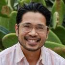 Person smiling with glasses against a cactus background.
